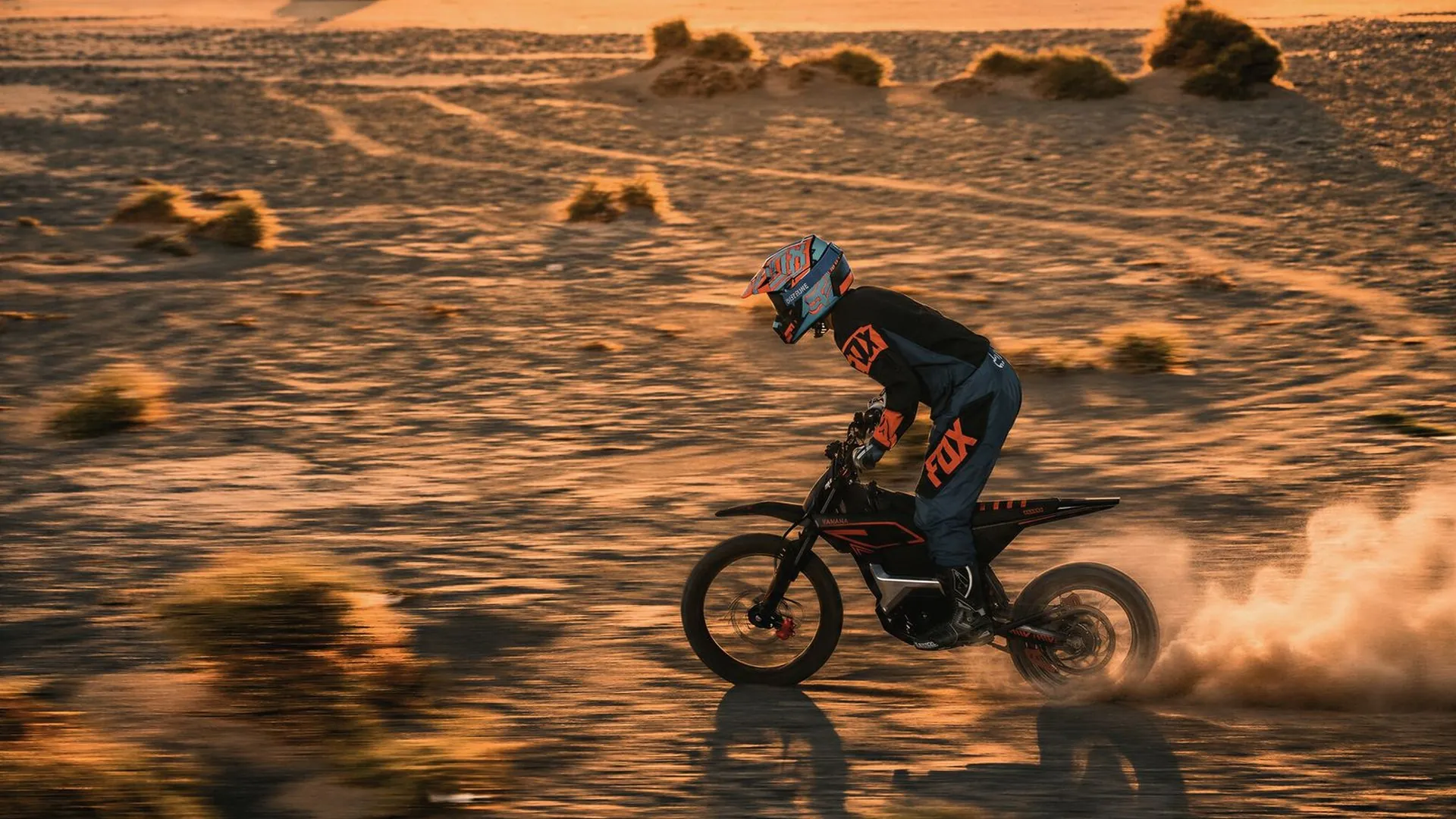 An adult rider on a full-size ARKAMOTO electric dirt bike at golden hour in the desert