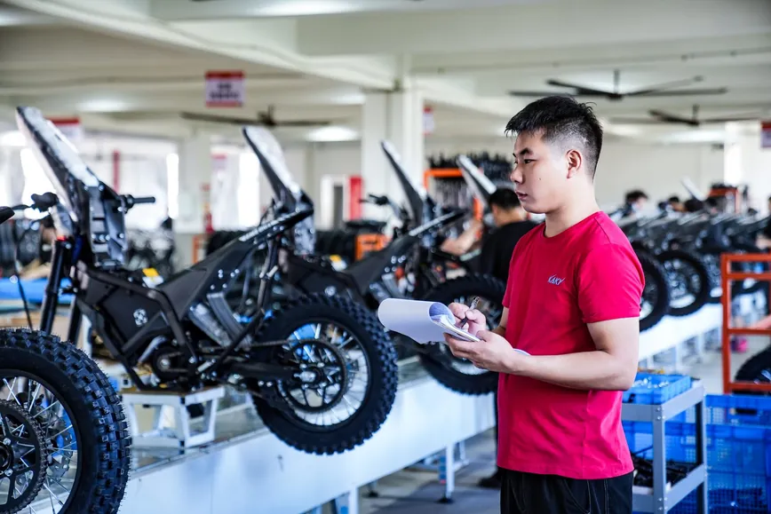 A technician checking a finished electric dirt bike against a checklist on the factory floor