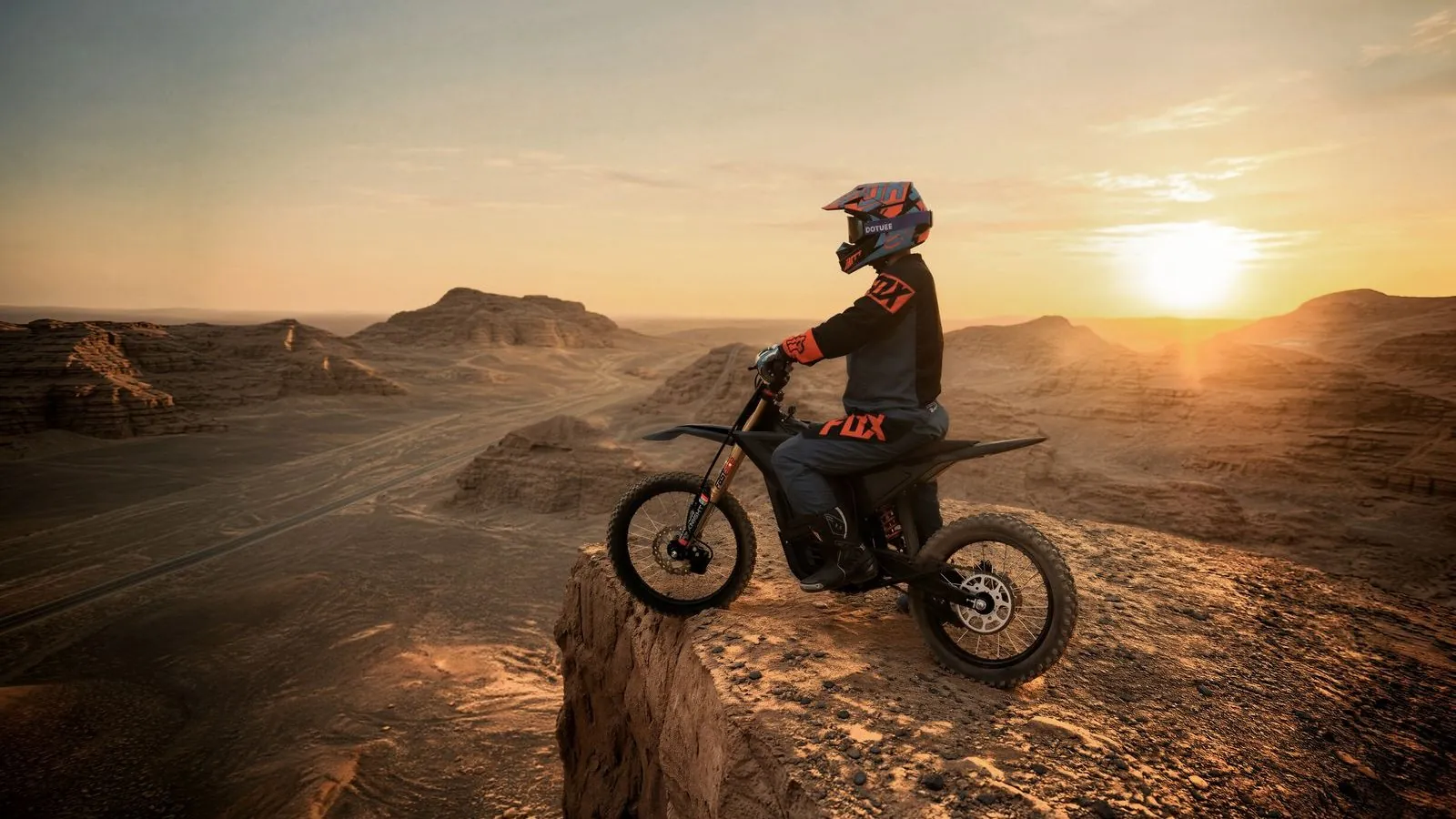 A rider on an ARKAMOTO youth electric dirt bike on a desert ridge at sunset
